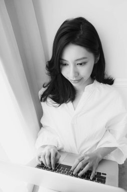 Genç Asyalı kadın evde siyah beyaz bilgisayar kullanıyor.