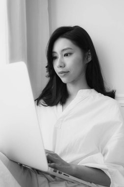 Genç Asyalı kadın evde siyah beyaz bilgisayar kullanıyor.