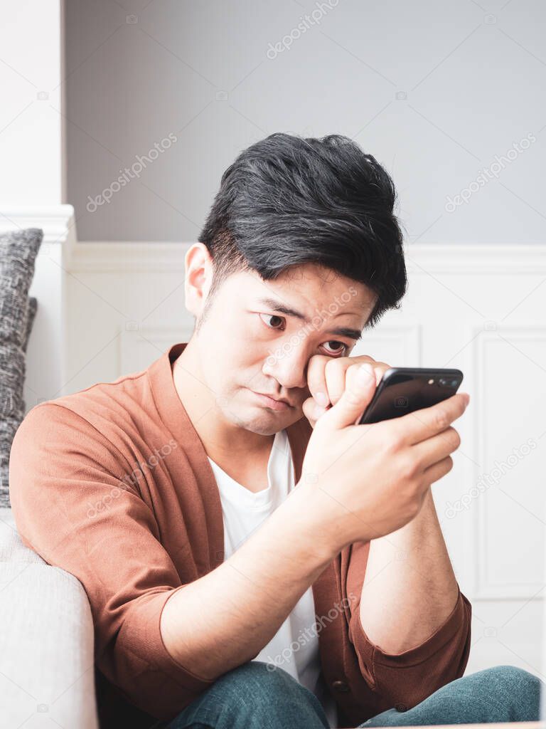 Asian young man rubbing his tired eyes his smartphone.