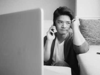 Asyalı genç adam yorgun gözlerini ovalıyor akıllı telefonunu..