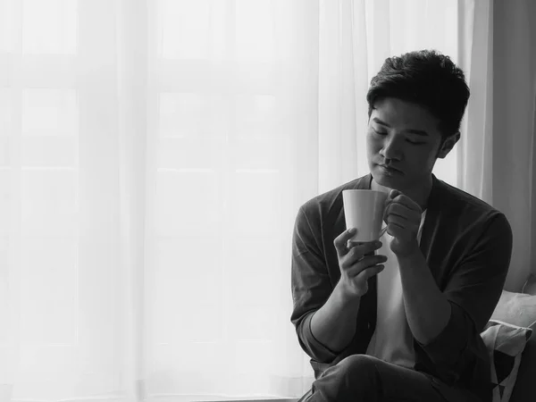 窓のカーテンの横の家で飲むハンサムな若い男 — ストック写真