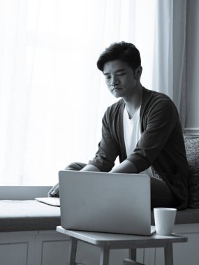 Asyalı genç adam dizüstü bilgisayarın önünde masada oturuyor.