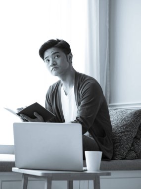 Asyalı genç adam dizüstü bilgisayarın önünde masada oturuyor.