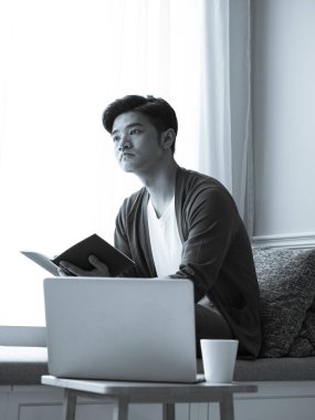 Asyalı genç adam dizüstü bilgisayarın önünde masada oturuyor.