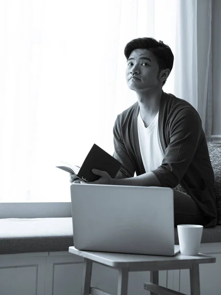 Asian young man sitting at the table in front of laptop computer