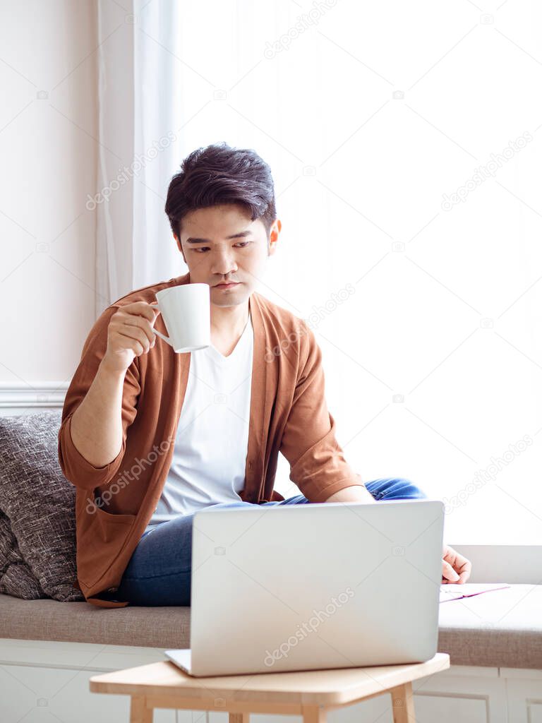 Asian young man sitting at the table in front of laptop computer