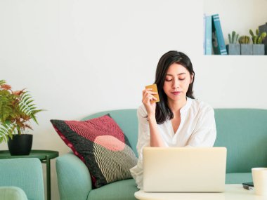 Genç bir kadın evde kredi kartı ve laptop ile online alışveriş yapıyor.