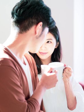 Genç Asyalı kadın ve erkek ellerinde bir fincan kahveyle evde vakit geçirmekten zevk alıyorlar..