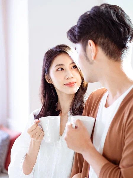 Genç Asyalı kadın ve erkek ellerinde bir fincan kahveyle evde vakit geçirmekten zevk alıyorlar..