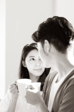 Genç Asyalı kadın ve erkek ellerinde bir fincan kahveyle evde..