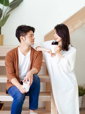 Genç Asyalı kadın ve erkek ellerinde bir fincan kahveyle evde vakit geçirmekten zevk alıyorlar..