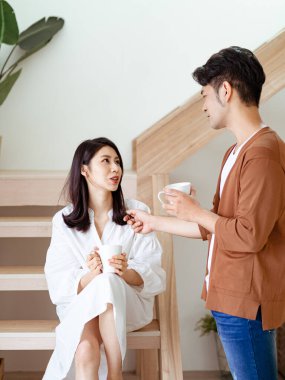 Genç Asyalı kadın ve erkek ellerinde bir fincan kahveyle evde vakit geçirmekten zevk alıyorlar..