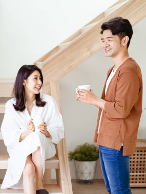 Genç Asyalı kadın ve erkek ellerinde bir fincan kahveyle evde vakit geçirmekten zevk alıyorlar..