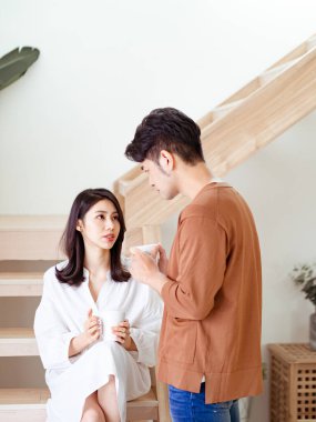 Genç Asyalı kadın ve erkek ellerinde bir fincan kahveyle evde vakit geçirmekten zevk alıyorlar..