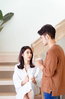 Genç Asyalı kadın ve erkek ellerinde bir fincan kahveyle evde vakit geçirmekten zevk alıyorlar..