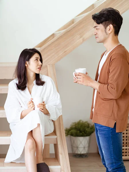 Genç Asyalı kadın ve erkek ellerinde bir fincan kahveyle evde vakit geçirmekten zevk alıyorlar..