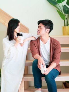 Genç Asyalı kadın ve erkek ellerinde bir fincan kahveyle evde vakit geçirmekten zevk alıyorlar..