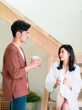 Genç Asyalı kadın ve erkek ellerinde bir fincan kahveyle evde vakit geçirmekten zevk alıyorlar..