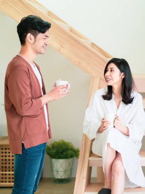 Genç Asyalı kadın ve erkek ellerinde bir fincan kahveyle evde vakit geçirmekten zevk alıyorlar..