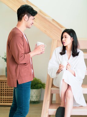 Genç Asyalı kadın ve erkek ellerinde bir fincan kahveyle evde vakit geçirmekten zevk alıyorlar..