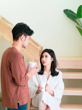 Genç Asyalı kadın ve erkek ellerinde bir fincan kahveyle evde vakit geçirmekten zevk alıyorlar..