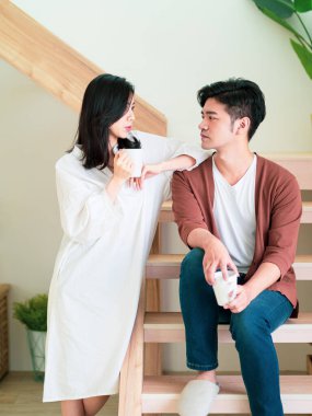 Genç Asyalı kadın ve erkek ellerinde bir fincan kahveyle evde vakit geçirmekten zevk alıyorlar..