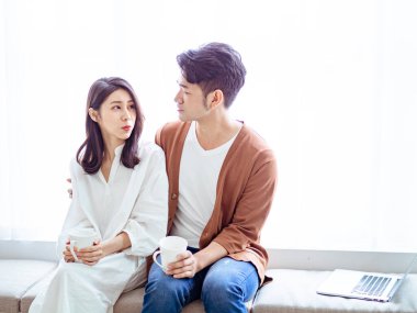 Genç Asyalı kadın ve adam ellerinde bir fincan kahveyle evde..