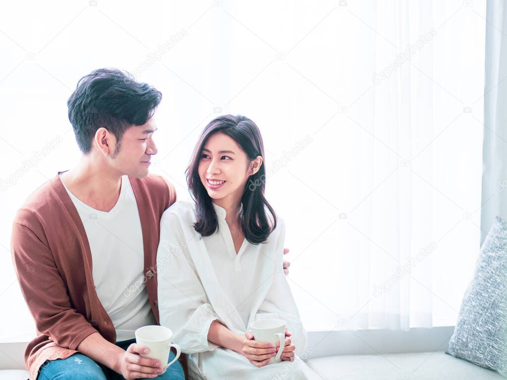 Young asian woman and man at home with cup of coffee in hands.