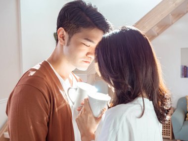 Genç Asyalı kadın ve erkek ellerinde bir fincan kahveyle evde vakit geçirmekten zevk alıyorlar..