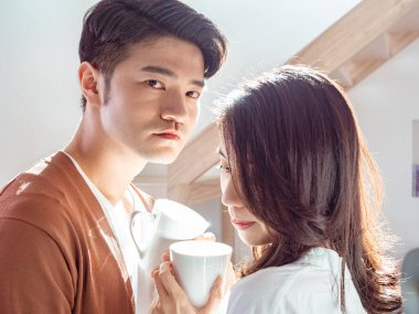 Genç Asyalı kadın ve erkek ellerinde bir fincan kahveyle evde vakit geçirmekten zevk alıyorlar..
