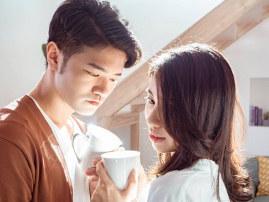 Genç Asyalı kadın ve erkek ellerinde bir fincan kahveyle evde vakit geçirmekten zevk alıyorlar..