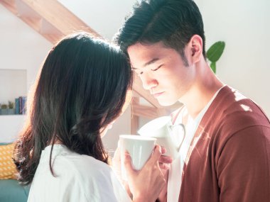 Genç Asyalı erkek ve kadın ellerinde bir fincan kahveyle evde..