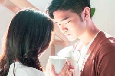 Genç Asyalı erkek ve kadın ellerinde bir fincan kahveyle evde..