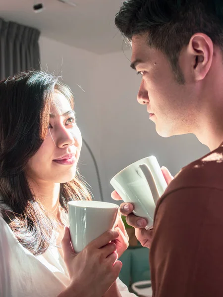 Genç Asyalı erkek ve kadın ellerinde bir fincan kahveyle evde..