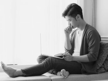 Genç Asyalı adam dizüstü bilgisayar kullanırken bir kitap yazıyor.