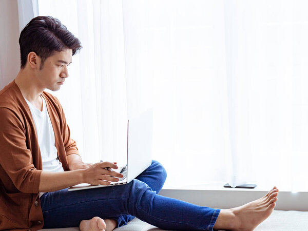 Young Asian man writing in a book when using laptop
