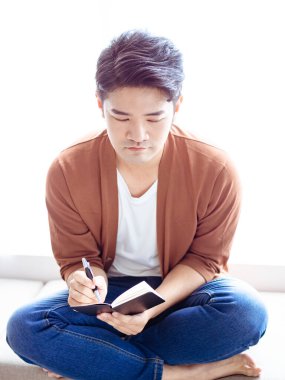 Not defterine yazı yazan çapraz bacaklı genç Asyalı..