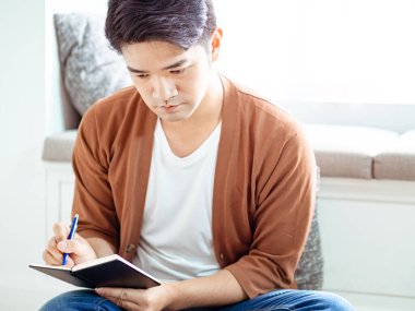 Not defterine yazı yazan çapraz bacaklı genç Asyalı..