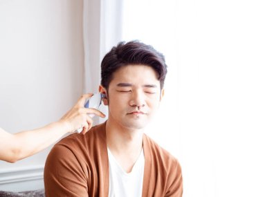 Genç Asyalı adam cerrahi maske takıyor ve kulak termometresi kullanıyor.