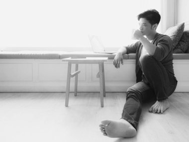 Genç Asyalı adam günlük kıyafetler giyiyor ve dizüstü bilgisayar kullanıyor.