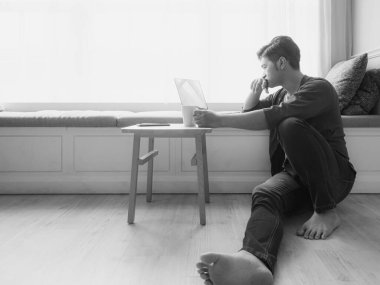 Genç Asyalı adam günlük kıyafetler giyiyor ve dizüstü bilgisayar kullanıyor.