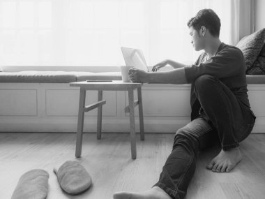 Genç Asyalı adam günlük kıyafetler giyiyor ve dizüstü bilgisayar kullanıyor.