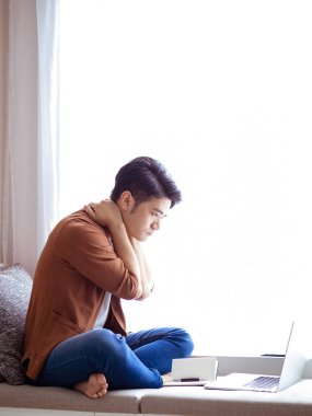 Genç Asyalı adam deftere yazı yazıyor ve dizüstü bilgisayar kullanıyor..