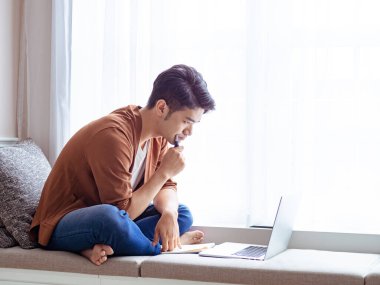 Genç Asyalı adam deftere yazı yazıyor ve dizüstü bilgisayar kullanıyor..