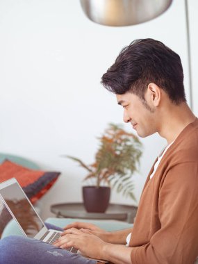 Genç Asyalı adam günlük kıyafetler giyiyor ve dizüstü bilgisayar kullanıyor.