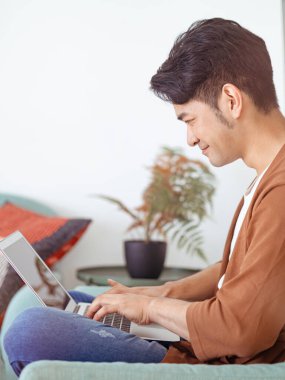 Genç Asyalı adam günlük kıyafetler giyiyor ve dizüstü bilgisayar kullanıyor.