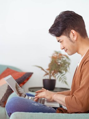 Genç Asyalı adam günlük kıyafetler giyiyor ve dizüstü bilgisayar kullanıyor.