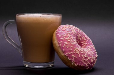 Şeffaf cam bardak kahve ve pembe çörek Menekşe arka plan üzerinde. Parlak sesi, yumuşak odak