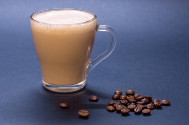 Şeffaf cam fincan kahve ve kahve çekirdekleri üzerinde mavi arka plan ile. Parlak sesi, yumuşak odak.