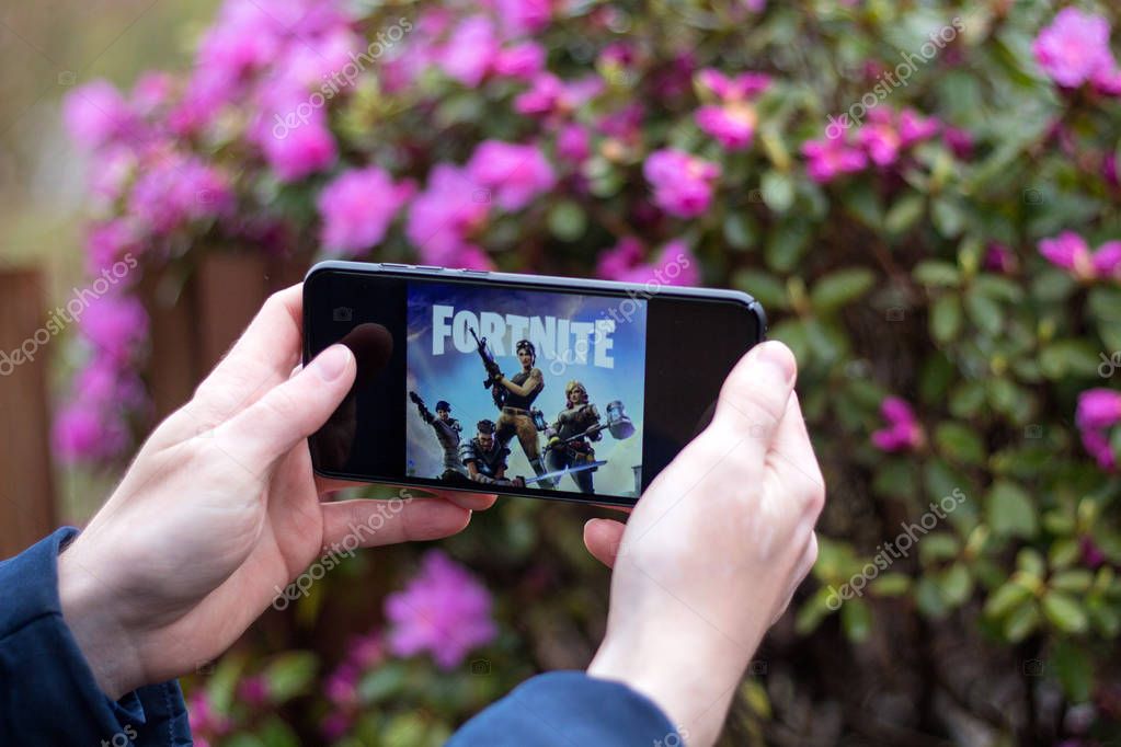 Saint Petersburg, RUSSIA -02 May, 2019: Popular fortnight game on mobile screen. A young guy in the park plays a fortnight.